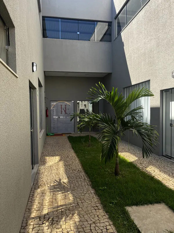 Corredor de entrada com pedras portuguesas, grama e uma palmeira, levando até a porta de vidro com o logo KE